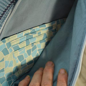 K&ouml;nnte beinhalten: Nahaufnahme einer blauen und grauen Stofftasche mit Rei&szlig;verschluss. Der Innenraum zeigt eine gemusterte Tasche mit blauen und gr&uuml;nen Mosaikfliesen. Das Futter der Tasche ist einfarbig hellblau.