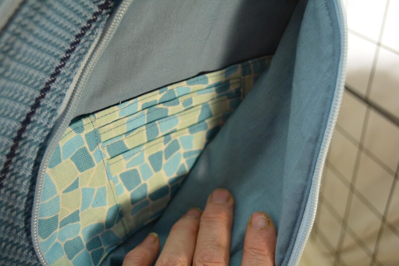 K&ouml;nnte beinhalten: Nahaufnahme einer blauen und grauen Stofftasche mit Rei&szlig;verschluss. Der Innenraum zeigt eine gemusterte Tasche mit blauen und gr&uuml;nen Mosaikfliesen. Das Futter der Tasche ist einfarbig hellblau.