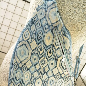 K&ouml;nnte beinhalten: Eine Sling-Tasche mit blauem und cremefarbenem geometrischem Muster mit einem Jeans-Tr&auml;ger und Rei&szlig;verschluss. Die Tasche hat ein sich wiederholendes Muster aus Sechsecken, Rauten und anderen Formen. Der Rei&szlig;verschluss ist silberfarben.