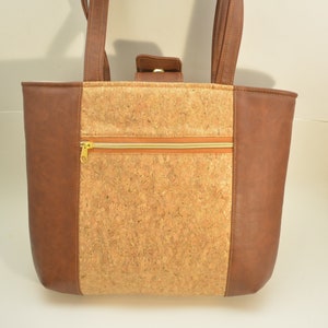 May include: A brown tote bag with a cork fabric panel and a zippered pocket. The bag has brown leather trim and a gold zipper.