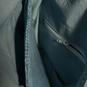 K&ouml;nnte beinhalten: Nahaufnahme des Innenraums einer hellblauen Handtasche. Die Tasche hat eine Rei&szlig;verschlusstasche und mehrere F&auml;cher. Der Stoff hat einen dezenten Glanz, und der Rei&szlig;verschluss ist silberfarben. Das Design deutet auf ein praktisches und stilvolles Accessoire hin.