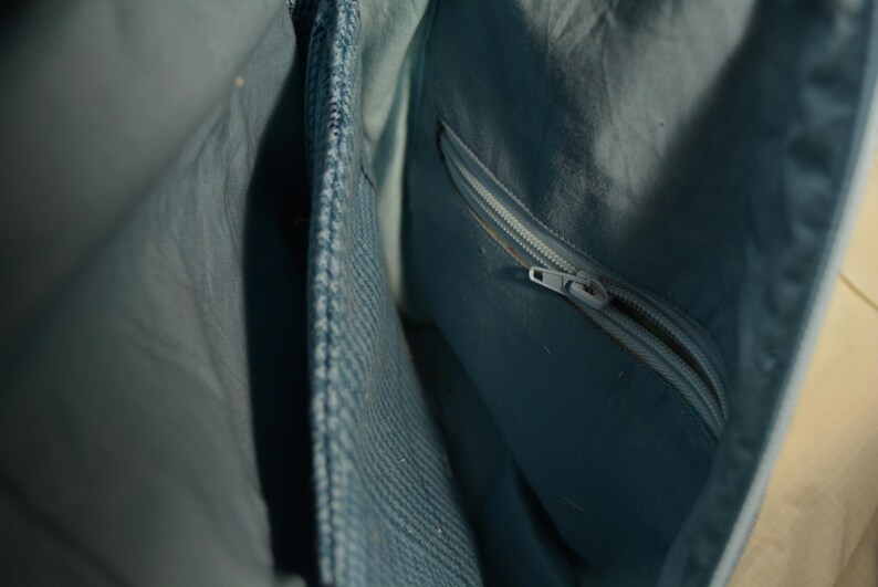 K&ouml;nnte beinhalten: Nahaufnahme des Innenraums einer hellblauen Handtasche. Die Tasche hat eine Rei&szlig;verschlusstasche und mehrere F&auml;cher. Der Stoff hat einen dezenten Glanz, und der Rei&szlig;verschluss ist silberfarben. Das Design deutet auf ein praktisches und stilvolles Accessoire hin.