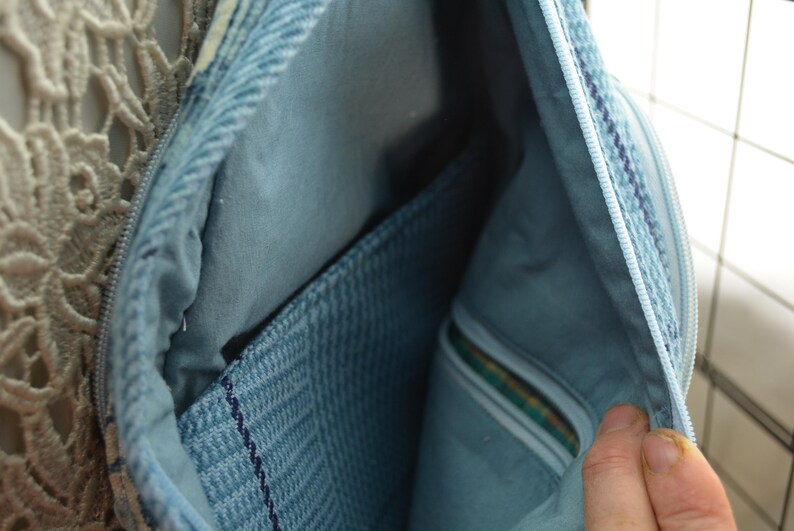 K&ouml;nnte beinhalten: Offene Ansicht einer hellblauen Jeans-Tasche, die das Innere zeigt. Die Tasche hat einen Rei&szlig;verschluss und ein hellblaues Futter. Es gibt eine Tasche aus strukturiertem Jeansstoff. Die Tasche ist offen und zeigt das Innere.