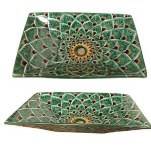 Op de afbeelding: Een groene keramische wastafel met een decoratief bloemenpatroon. De wastafel heeft een vierkante vorm met afgeronde hoeken en een afvoergat in het midden.