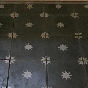 May include: A close-up of a floor with a repeating pattern of white stars on dark gray tiles.