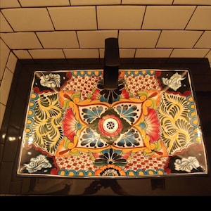 May include: A colorful ceramic sink with a floral design in shades of blue, green, yellow, red, and black. The sink has a black faucet and a white drain.