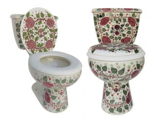 Op de afbeelding: Een keramische toiletset met een crèmekleurige basis, versierd met een herhalend patroon van rode rozen, groene bladeren en kleine rode hartjes. De set bestaat uit een toiletpot, een reservoir en een bijpassende toiletbril met bloemmotief.