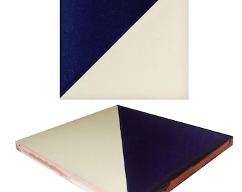 May include: A square ceramic tile featuring a diagonal split design with one half in deep navy blue and the other half in off-white. The tile has a smooth, glossy finish on the top surface and a visible terracotta-colored clay base edge.