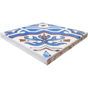May include: A white ceramic tile featuring a blue and red floral pattern. The tile has a geometric design with a central flower motif.