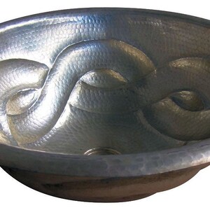 May include: A silver hammered copper vessel sink with a decorative, interwoven design. The sink is round and has a smooth, polished finish.