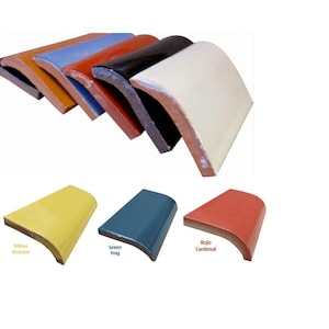 Op de afbeelding: Assortiment van gebogen keramische tegels in verschillende kleuren, waaronder geel, blauw, rood, zwart en wit. De tegels zijn in een halve cirkel gerangschikt, met de witte tegel bovenaan.