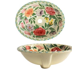 Könnte beinhalten: Ein weißes Keramik-Waschbecken mit floralem Design. Das Waschbecken ist rund und hat ein einzelnes Abflussloch. Das Blumenmuster zeigt rosa, rote, gelbe und blaue Blumen auf grünem Hintergrund.