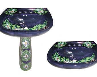 May include: A dark blue ceramic pedestal sink and a matching drop-in sink basin, both featuring a hand-painted pattern of white calla lilies with green leaves. The pedestal sink has a tall base, while the basin has three faucet holes.