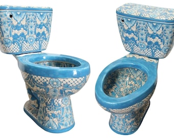 Op de afbeelding: Twee keramische toiletten met een levendig blauw en wit bloemenpatroon. Elk toilet heeft een bijpassende blauwe zitting, een reservoir met deksel en een voetstuk dat is versierd met complexe botanische motieven en rasterpatronen.