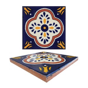 May include: Square ceramic tile with a floral design. The tile has a navy blue background with a white, orange, and yellow floral pattern. The tile is shown from two angles, one flat and one at an angle.