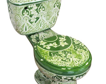Op de afbeelding: Een keramisch toilet met een glanzende afwerking en een ingewikkeld wit en groen botanisch patroon dat de gehele buitenkant bedekt, inclusief het reservoir, de pot en de bijpassende ronde toiletbril.