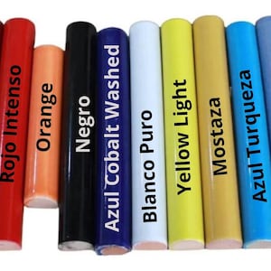 Puede incluir: Una colección de veinte varillas cilíndricas dispuestas en fila, cada una con un color sólido distinto y una etiqueta impresa. Los colores incluyen tonos de rojo, amarillo, blanco, azul, violeta, naranja, negro, mostaza, marrón, verde y chocolate.