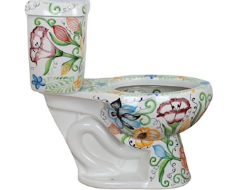 Op de afbeelding: Een wit keramisch toilet met een handgeschilderd bloemmotief in rood, oranje, blauw en groen. Het patroon bestaat uit gestileerde bloemen, bladeren en krullende ranken die het reservoir, de pot en de rand van de zitting sieren.