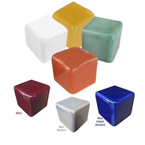 Op de afbeelding: Assortiment van keramische glazuurmonsters in verschillende kleuren, waaronder wit, geel, groen, oranje, rood, blauw en grijs. De monsters zijn in de vorm van kleine kubussen.