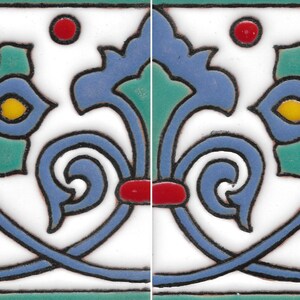 May include: A rectangular ceramic tile featuring a repeating border pattern with a white background. The design includes blue floral motifs with yellow centers, green accents, and small red circular details, all outlined in a dark black line.