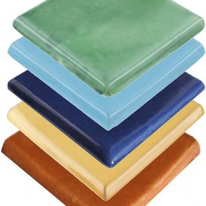 Può includere: Una pila di piastrelle quadrate in ceramica di vari colori. Le piastrelle sono disposte in una pila diagonale, mostrando sfumature di verde, azzurro, blu navy, giallo e marrone. Ogni piastrella ha una finitura lucida e bordi arrotondati.