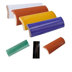 Op de afbeelding: Assortiment van keramische tegelprofielen in verschillende kleuren, waaronder wit, oranje, geel, blauw en groen. De tegelprofielen zijn gebogen en hebben een afgeronde rand.