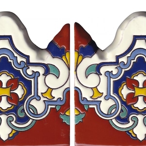 May include: Two rectangular ceramic tiles featuring a scalloped top edge. The surface displays a symmetrical pattern with a central red and yellow floral motif, surrounded by intricate blue, white, and teal scrollwork against a deep red base.