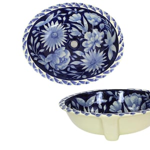 May include: Two ceramic bathroom sinks. The sinks are oval-shaped with a cream exterior and a blue floral interior design. The rims are decorated with a blue leaf pattern. The sinks are designed for drop-in installation.