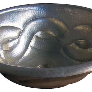 May include: A silver hammered copper sink with a decorative design of interwoven swirls. The sink is round and has a smooth, polished finish.