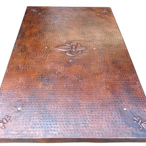 May include: A rectangular copper table top with a hammered texture and a fleur-de-lis design in the center. The corners feature fleur-de-lis designs. The table top has a rich, warm brown color with darker areas.