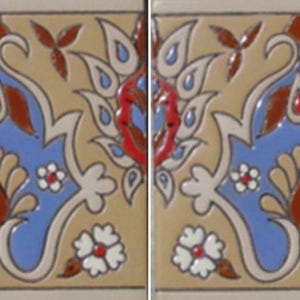 May include: A square ceramic tile featuring a symmetrical floral pattern in shades of blue, tan, red, and white. The design includes a central blue leaf-like shape with tan petals, surrounded by red and white floral accents on a tan background.