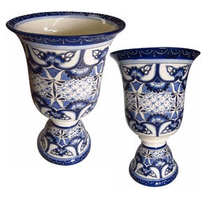 May include: Two blue and white ceramic vases with intricate floral patterns. The larger vase has a wider base and a more rounded shape. The smaller vase has a narrower base and a more cylindrical shape.