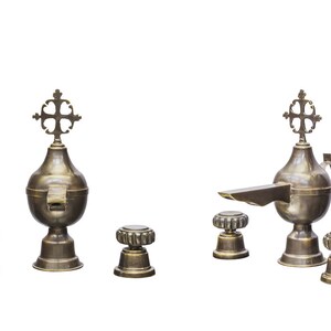 May include: A set of five antique brass religious oil lamps with cross finials. The lamps are in various sizes and shapes, with one featuring a spout. The lamps are arranged on a white background.