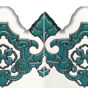 May include: Two identical ceramic tiles featuring a scalloped top edge and a white base color. Each tile displays a raised, intricate teal-colored pattern with symmetrical scrollwork and a central four-petaled floral motif in relief.