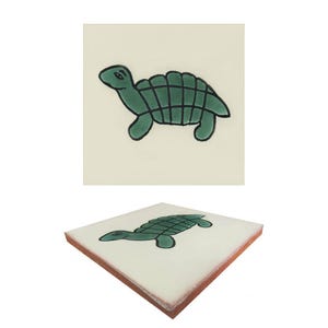 May include: A square ceramic tile featuring a green cartoon turtle design. The turtle has a green shell with black grid lines, green head, and green legs. The tile has a cream-colored background and a brown edge.