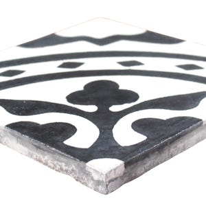 May include: Black and white ceramic tile with a geometric pattern. The tile has a distressed look and features a floral design.