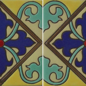 May include: Two square ceramic tiles featuring a central dark blue fleur-de-lis motif inside a brown diamond border. The design includes a small red circle at the center, light teal scrollwork accents, and a solid yellow background color.