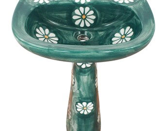 May include: A dark green ceramic pedestal sink featuring a hand-painted white daisy pattern with yellow centers. The basin has a wide, curved rim and a central drain hole, while the pedestal base is decorated with matching floral motifs throughout.