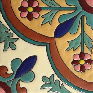 May include: Square ceramic tile with a floral design. The tile features a cream-colored background with a repeating pattern of flowers, leaves, and geometric shapes in shades of pink, yellow, blue, green, and brown. The design is outlined in black.