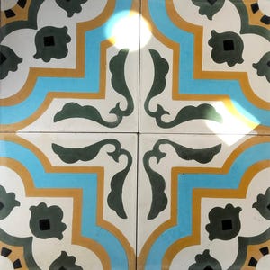May include: Four square tiles arranged together, featuring a repeating pattern. The design includes a white background with teal, gold, and blue geometric shapes. Dark green leaf-like shapes and black squares complete the pattern, creating a decorative tile design.