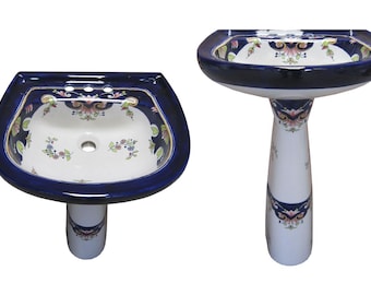 May include: A ceramic pedestal sink featuring a white basin with a deep blue rim and floral patterns in pink, green, and blue. The basin includes three faucet holes and a central drain. The pedestal base is white with matching blue and floral accents.