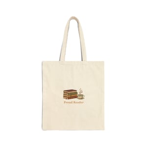 Peut inclure: Sac fourre-tout crème avec un motif représentant une pile de livres, une tasse de café et les mots "Proud Reader". Le sac a deux anses et est fait d'une matière semblable à de la toile. Le motif est dans les tons de brun et beige.