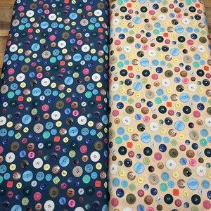 May include: Two bolts of fabric featuring a dense, all-over print of round buttons in various sizes and colors. One bolt has a dark navy blue background, while the other has a light tan background. Both fabrics display a repeating pattern of buttons.