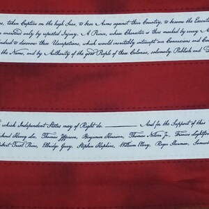May include: Close-up of a red and white fabric with handwritten text. The text is in black cursive and appears to be a historical document. The fabric has red stripes and white bands with text.