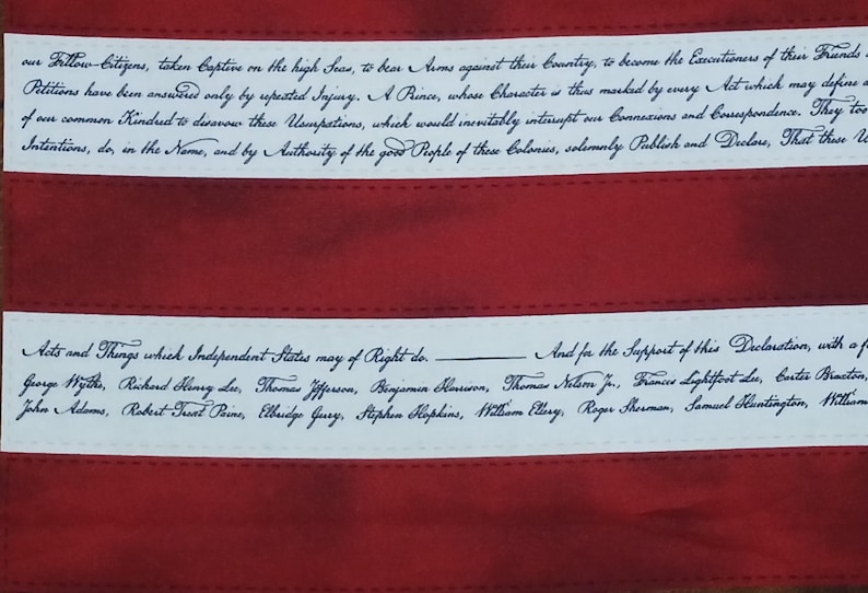 May include: Close-up of a red and white fabric with handwritten text. The text is in black cursive and appears to be a historical document. The fabric has red stripes and white bands with text.