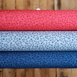May include: Three rolls of fabric with a star pattern. The top roll is red with white stars, the middle roll is light blue with dark blue stars, and the bottom roll is dark blue with white stars.