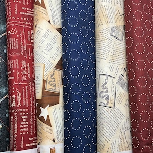 May include: A collection of fabric rolls with patriotic and historical designs. Patterns include cannons, text, stars, and circles. Colors include navy, red, tan, and white. Some rolls feature text like "We the People" and "Join or Die."