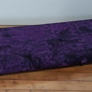 May include: Purple fabric with a black and white tie-dye pattern. The fabric is folded in half and lying on a wooden surface.
