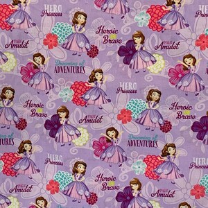 May include: Purple fabric with a repeating pattern of a princess in a purple dress, flowers, and the text "Magic Amulet", "Hero Princess", "Heroic Brave", and "Dreaming of Adventures".