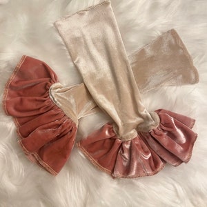 May include: A pair of velvet arm warmers with a ruffled trim. One arm warmer is beige and the other is a dusty rose color.